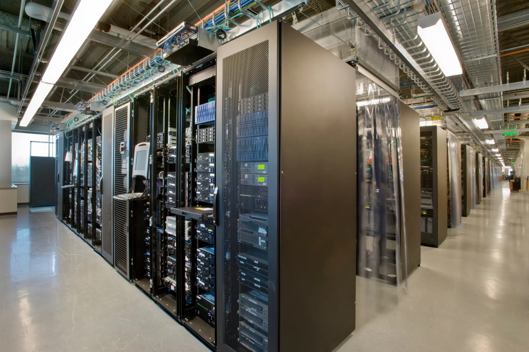 Rows of server racks in a modern data center with network cables and cooling systems.